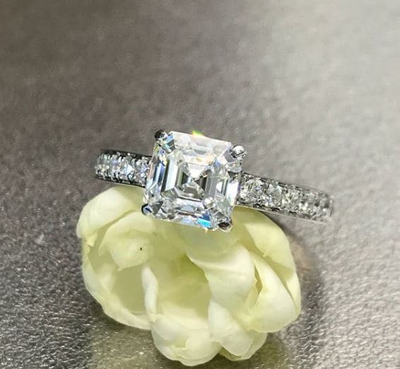 Asscher cut diamond set in a low prong solitaire with pave diamonds in the band